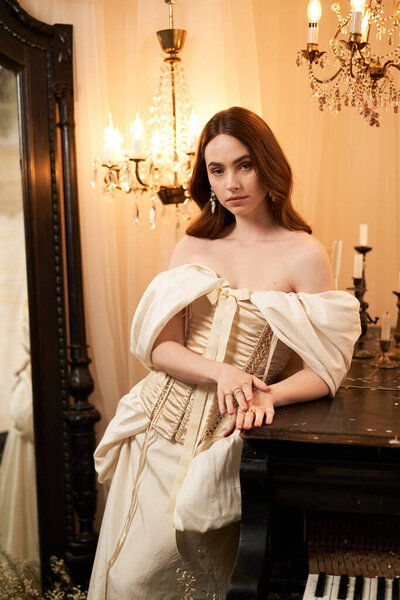 Красивая молодая женщина изящно стоит в винтажном платье, окруженная мягким свечой.