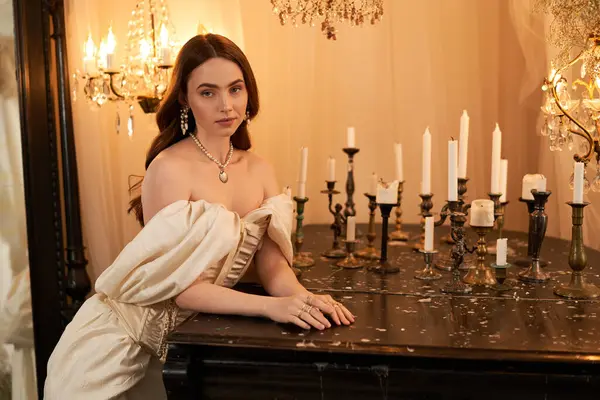 Güzel genç bir kadın zarif bir klasik elbiseyle poz verir, mum ışığıyla aydınlatılır..