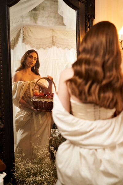 A young woman in an exquisite vintage dress holds a basket while gazing into a lavish mirror.