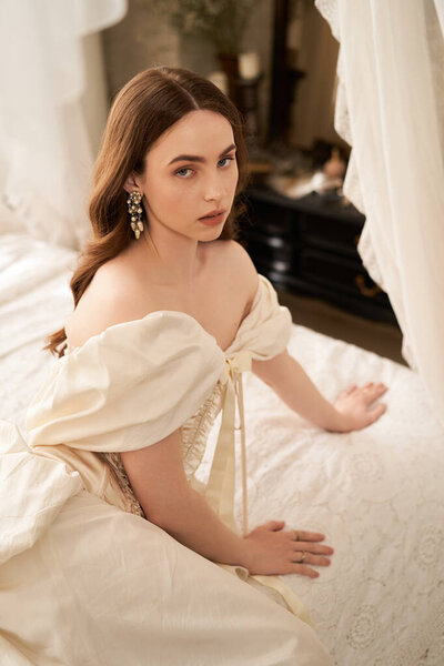 Красивая молодая женщина в винтажном платье изящно сидит у окна с мягким освещением, излучая элегантность..