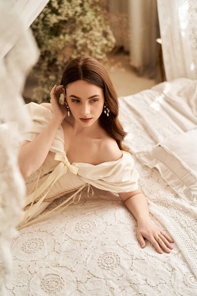 Молодая женщина элегантно расслабляется на кружевной кровати в винтажном платье.