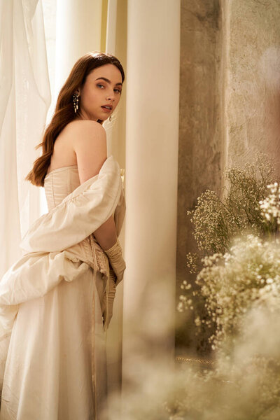 Очаровательная молодая женщина грациозно стоит в винтажном платье, окруженная нежными цветочными акцентами.