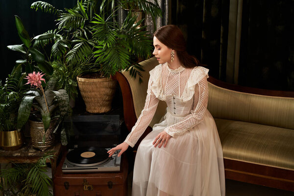 Красивая молодая женщина в винтажном платье нежно взаимодействует с проигрывателем среди зелени.