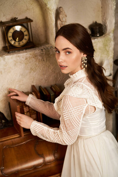 Красивая молодая женщина в винтажном платье с любопытством рассматривает старинные книги в уютной обстановке..