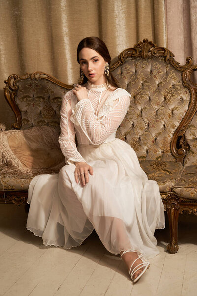 Элегантная молодая женщина сидит изящно, одетый в потрясающее винтажное платье, олицетворяющий красоту.