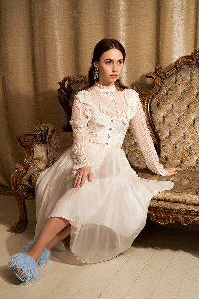 Прекрасная молодая женщина в нежном платье элегантно сидит на декоративной мебели, источая очарование.