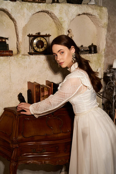 Красивая молодая женщина в винтажном платье принимает позу в уютной деревенской обстановке.