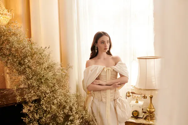 Güzel, genç bir kadın güneşli bir pencerenin yanında zarif bir şekilde duruyor, eski moda bir cazibe yayıyor..