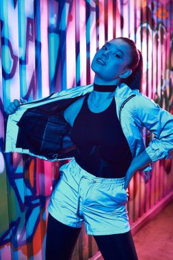 Güzel bir kadın benzersiz modasını gün batımında renkli, duvar yazısıyla dolu bir sokakta sergiliyor..