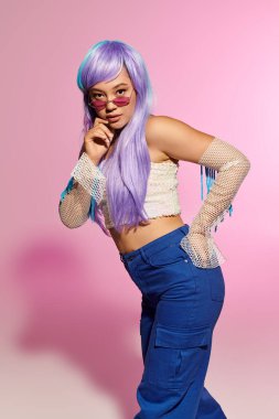 Mor saçlı şık bir kadın, fotoşoptaki pastel bir arka plana bakıyor..