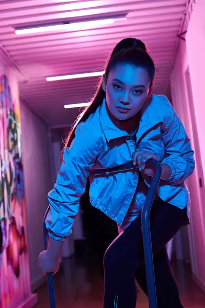 Şık bir kadın renkli, neon ışıklı bir koridorda cesur bir poz verir..