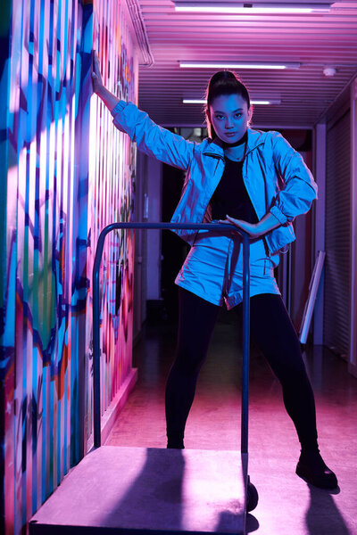 Уверенная женщина позирует в красочном коридоре, легко смешивая моду и творчество.