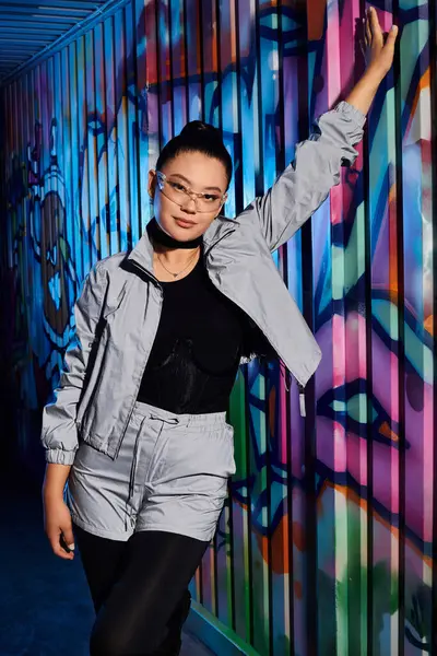 Şık bir kıyafet, kendine güvenen bir duruş ve çarpıcı gözlüklerle göze çarpıyor..