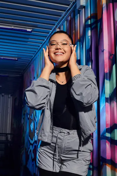 Heyecanlı genç kadın renkli duvar yazılarına karşı neşeli bir şekilde poz veriyor.