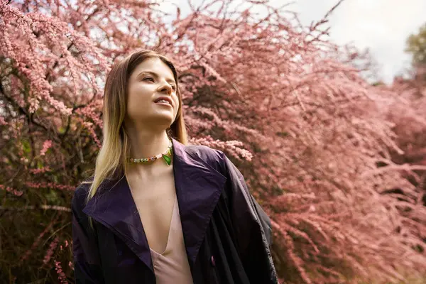 Pembe çiçekler ceketli bir kızı çerçeveler, bahar ışığına bakar..