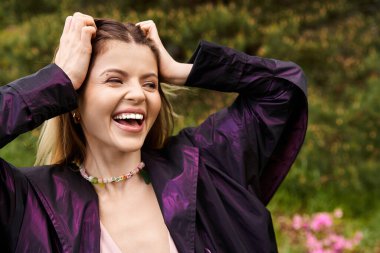 Genç bir kadın gülümsüyor, elleri saçlarında..