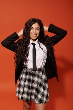 Neşeli genç bir öğrenci elleri saçında poz veriyor, modaya uygun kıyafetler giyiyor..