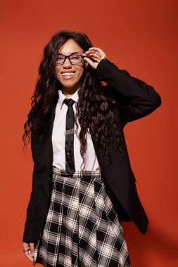 Güzel genç bir kadın, gözlüğünü şakayla ayarlarken modern öğrenci modasını sergiliyor..