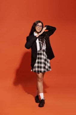 Uzun saçlı genç bir kadın şık elbisesini turuncuya karşı parlak ve neşeli bir tavırla sergiliyor..