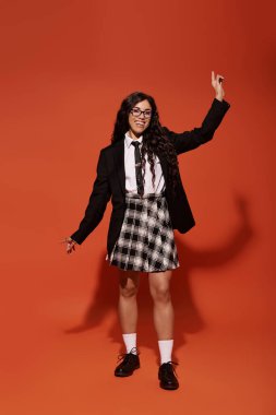 Şık, genç bir kadın şık bir okul elbisesiyle parlak bir arkaplana karşı poz veriyor..