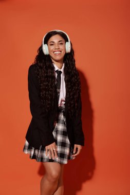 Genç bir kadın sıcak turuncu bir arkaplan karşısında şık bir okul kıyafetine güveniyor..