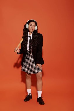 Güzel genç bir kadın cesur bir şekilde duruyor, eşsiz moda seçimini canlı bir ortamda sergiliyor..