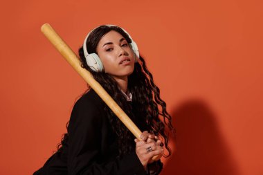 Güzel, genç bir öğrenci kendine güvenen bir şekilde yarasa ve kulaklıkla poz veriyor..