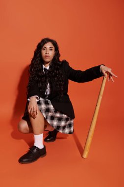 Şık bir öğrenci çarpıcı bir ortamda beyzbol sopasıyla diz çöker..