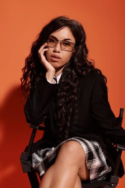 Genç bir kadın, çarpıcı bir arka planda rahat rahat otururken kendine güveni tam..