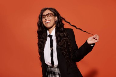 Öğrenci kıyafetli genç bir kadın gülümsüyor, uzun, siyah kıvırcık saçlarından bir tel tutuyor..