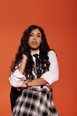 Kıvırcık saçlı, kendine güvenen genç bir kadın şık bir kıyafet içinde poz veriyor..