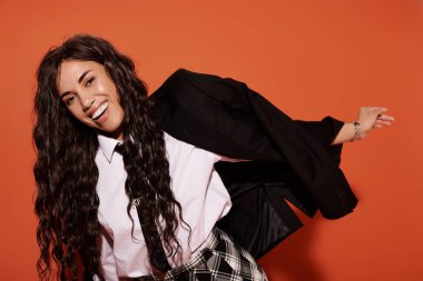 Genç bir kadın canlı turuncu bir arkaplan karşısında bir öğrenci titreşiminde neşe içinde poz veriyor..