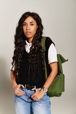 Dalgalı saçlı, günlük kıyafetleri olan genç bir öğrenci yaratıcı bir mekanda rahatça poz veriyor..