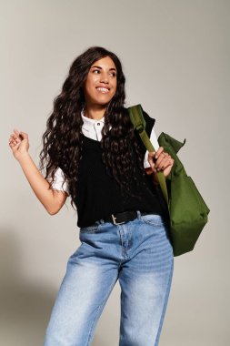 Kendinden emin genç bir kadın çantasını taşırken ve öğrenci enerjisi yayarken modaya uygun bir görünüm sergiliyor..