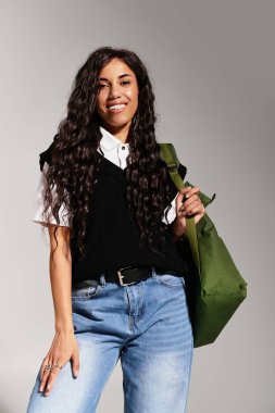 Gülümseyen genç kadın, güzel tarzını günlük kıyafetleri ve yeşil çantasıyla sergiliyor..