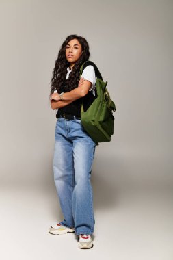 Kendine güvenen genç bir kadın, bir sırt çantasıyla ayakta dururken modaya uygun öğrenci tarzını sergiliyor..