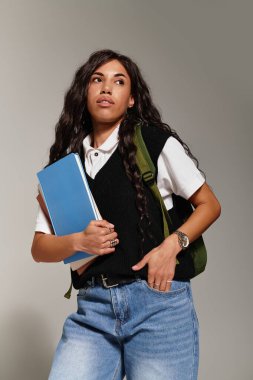 Güzel, genç bir kadın, elinde kitaplarla ve modaya uygun öğrenci tarzıyla kendine güvenerek ayakta duruyor..