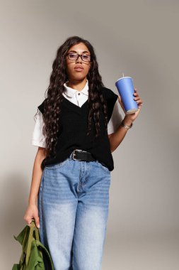 Kendine güvenen genç bir öğrenci moda anlayışını sergilerken ferahlatıcı bir içeceğin tadını çıkarıyor..