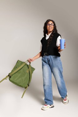 Parlak, neşeli öğrenci elinde bir içki ve bir çanta tutuyor, şık bir elbiseyle neşe saçıyor..