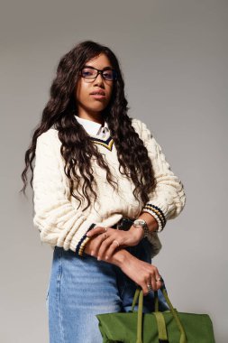 Havalı bir süveter içinde, rahat bir yerde yeşil bir çanta tutan çekici genç bir öğrenci..