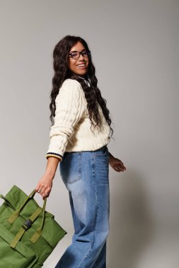 Şık giyinmiş kendine güvenen genç bir kadın, zarif bir şekilde içeride poz verirken yeşil bir çanta taşıyor..