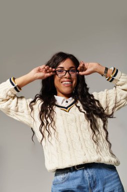Neşeli genç bir kadın rahat bir süveter ve gözlük giyer neşe içinde poz verir, pozitiflik saçar.