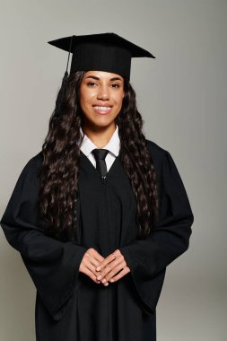 Mezuniyet şapkası ve cübbesi içinde, başarısından gurur duyan neşeli genç bir kadın..