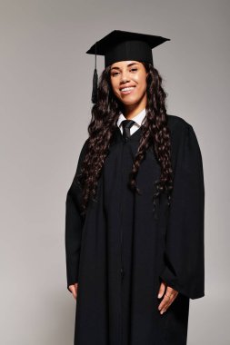 Mezuniyet elbisesi ve şapkası giymiş genç bir öğrenciden parlak bir gülümseme yayılıyor..