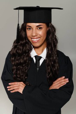Mezuniyet kıyafetli güzel bir kadın gururla poz verir, kollarını kavuşturur, gülümser..