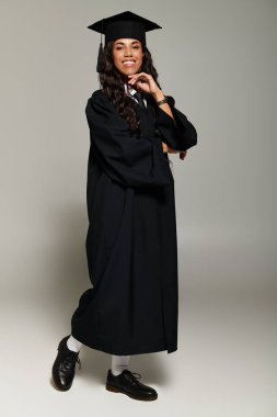 Genç bir kadın mezuniyet kıyafeti içinde gururla poz verir, mutluluk ve başarı saçar..