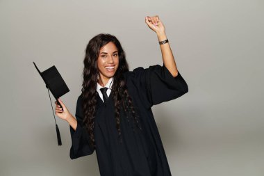 Mezuniyet elbisesi giymiş genç bir kadın akademik başarısını şapkasıyla kutluyor.