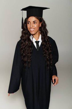 Mezuniyet elbisesi ve şapkası giymiş güzel genç bir kadın zarif bir şekilde yürür, mutluluk saçar..