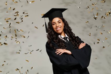 Mezuniyet kıyafetli genç bir kadın konfetiler etrafını sararken gururla gülümsüyor..