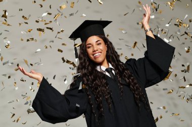Mezuniyet kıyafetli genç bir kadın konfeti düşerken sevinçle gülümsüyor..